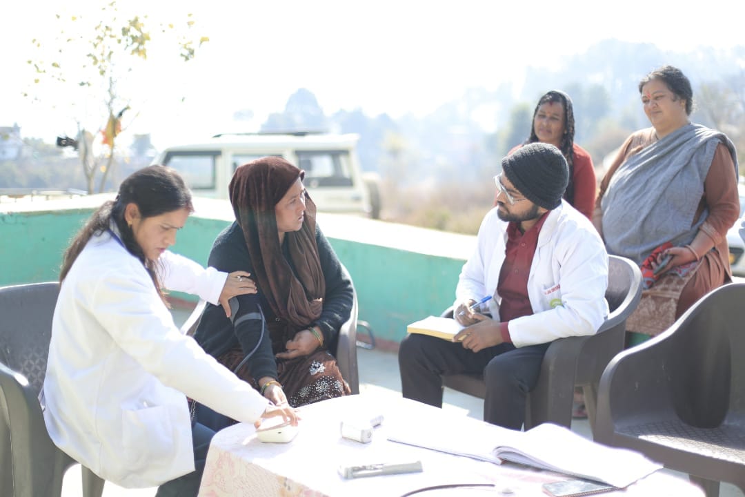 Woman getting blood pressure checkup at Seemant Sewa Foundation mobile medical unit while patients wait for OPD consultation in Uttarakhand village